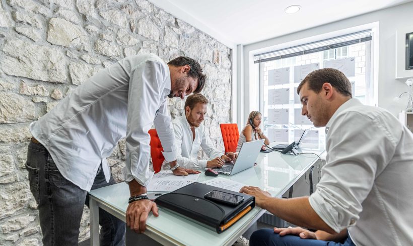 On aperçoit dans un bureau avec 4 collaborateurs dont une collaboratrice au téléphone assise devant son ordinateur portable en train d’avoir une conversation téléphonique.