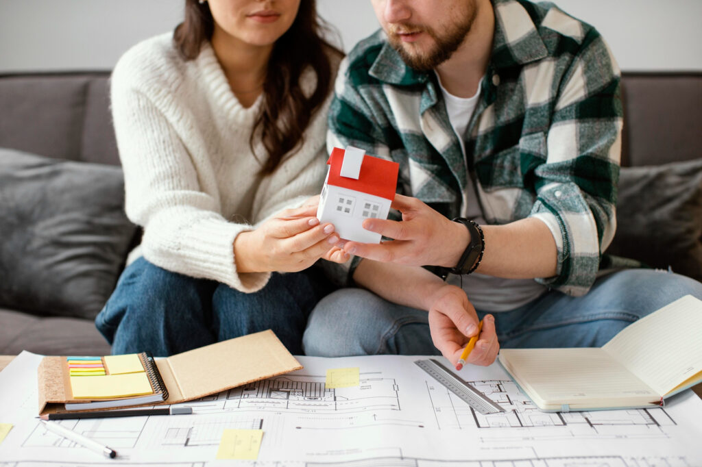 Couple comparant un projet de résidence principale et un investissement locatif autour d’une maquette de maison
